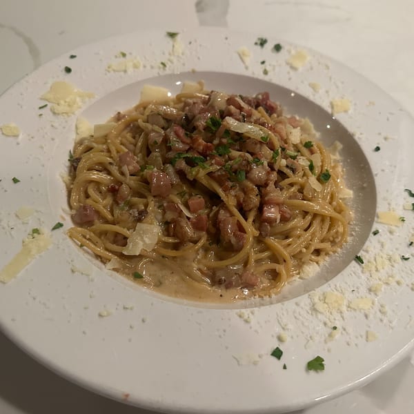 Spaghetti carbonara with bacon, parmesan cheese, and parsley on a white plate at Monica's Trattoria.