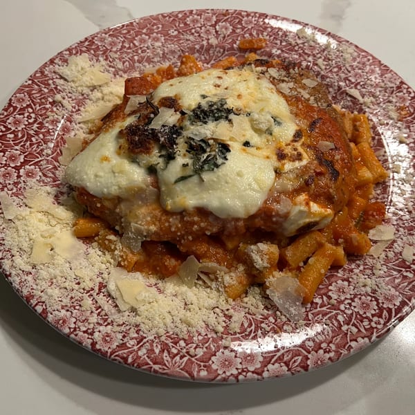Monica's Trattoria's baked ziti with melted cheese, tomato sauce, and grated parmesan on a red floral plate.