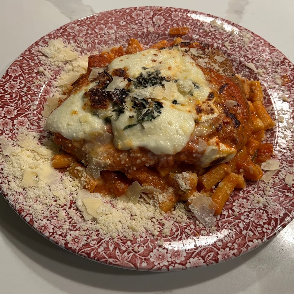 Monica's Trattoria's baked ziti with melted cheese, tomato sauce, and grated parmesan on a red floral plate.