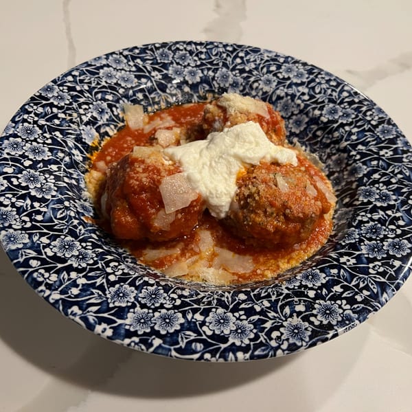Monica's Trattoria meatballs in red sauce with ricotta and parmesan cheese in a blue floral bowl.