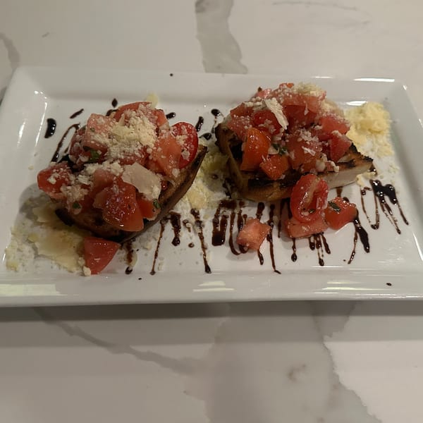 Two bruschetta pieces topped with diced tomatoes, grated cheese, and balsamic glaze on a white plate.