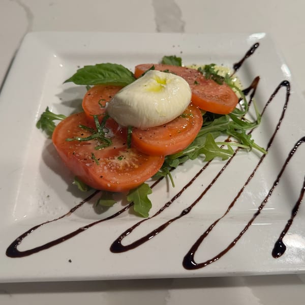 Caprese salad with sliced tomatoes, fresh mozzarella, basil, arugula, and balsamic glaze on a white plate.