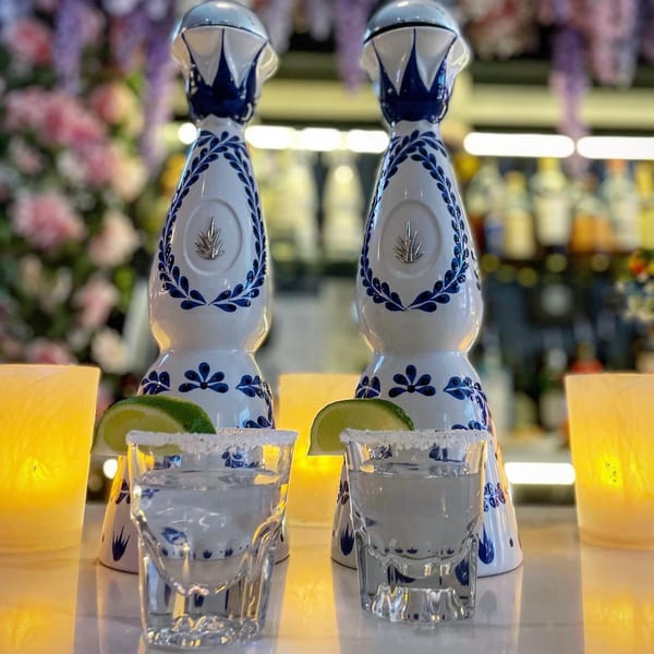 Two tequila bottles and two salt-rimmed margarita glasses with lime wedges on a bar.