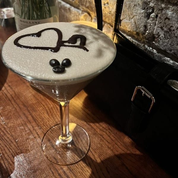 A martini glass with a frothy drink, decorated with a chocolate heart and coffee beans.