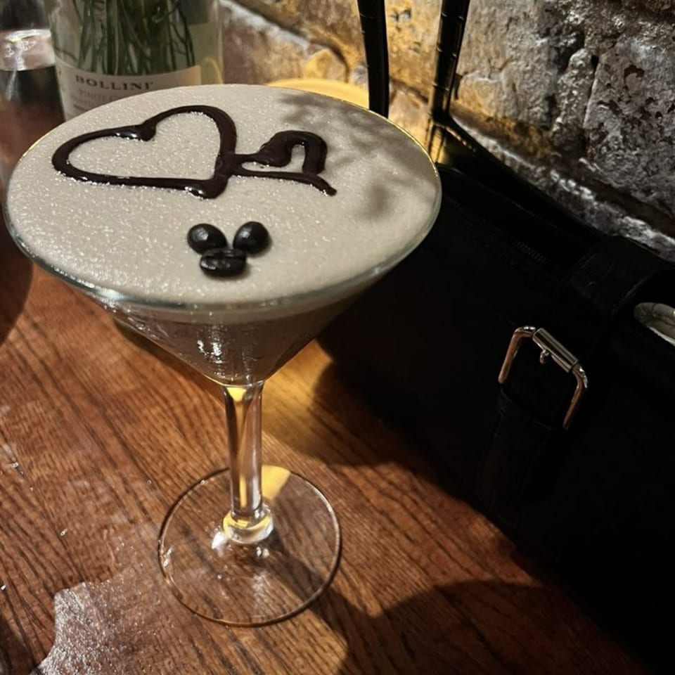 A martini glass with a frothy drink, decorated with a chocolate heart and coffee beans.